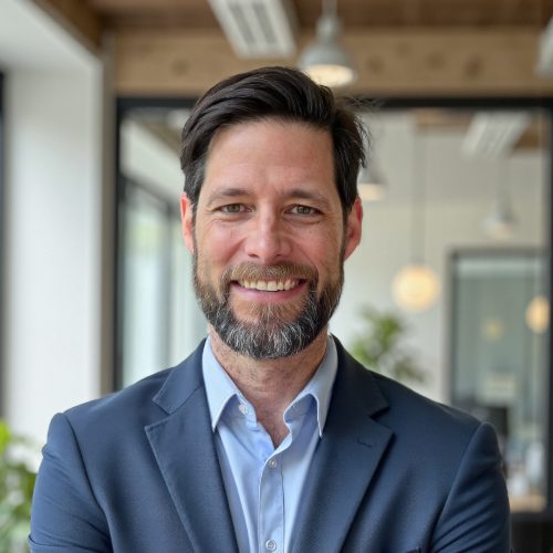Rob Boothe Professional businessman smiling in modern office environment, wearing a navy suit and light blue sh.