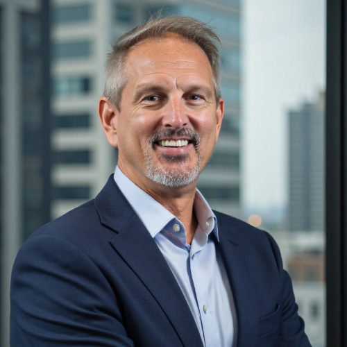 Jamey Forness CEO of The ProMedia Group smiling in a professional office setting with cityscape background.