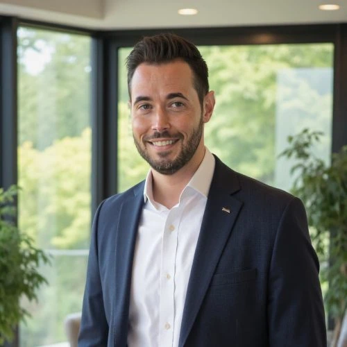 Brent Avis Professional businessman smiling in modern office with large windows and greenery outside.